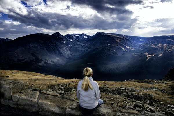 Mujer sentada frente a unas montañas nevadas en posición de meditación Mindfulness.