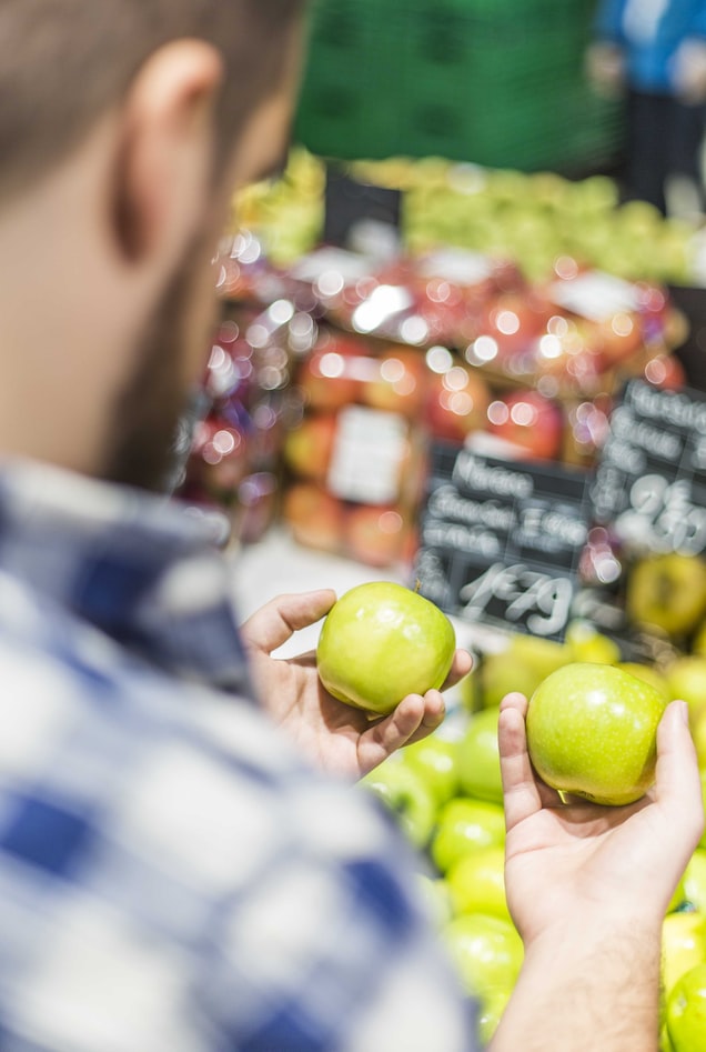 Hombre en el supermercado con una manzana verde en cada mano. Como tomar decisiones.