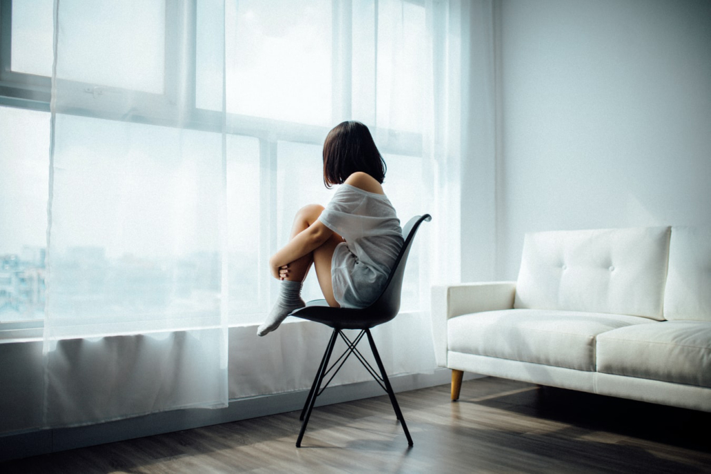 Chica joven mirando pensativa y triste por la ventana.